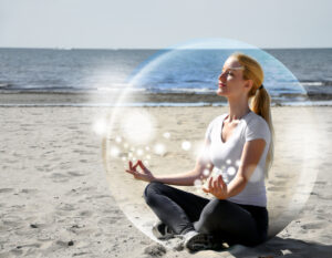 A woman is sitting on the beach inside a bubble with peace and tranquility. She is meditating and there are sparkles.